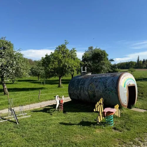 Spielplatz mit Tonnenhaus und Federwippen auf der Wiese