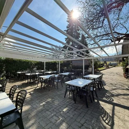 Terrasse mit Tischen und Stühlen unter der Pergola