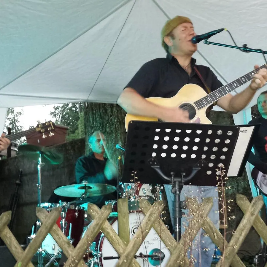Sänger mit Gitarre und Band beim Konzert im Garten